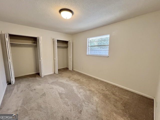 unfurnished bedroom with two closets, light carpet, and a textured ceiling