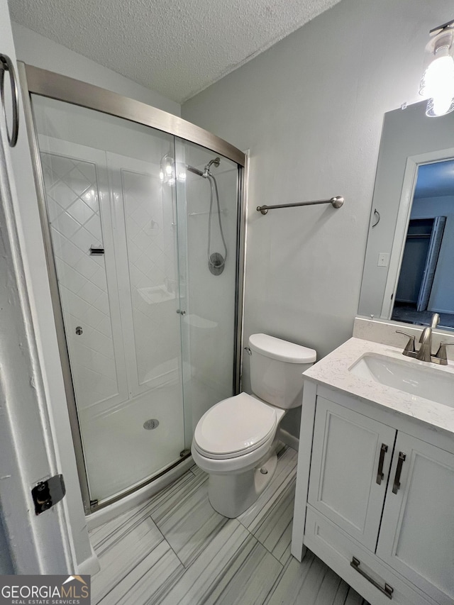 bathroom featuring toilet, a textured ceiling, a shower with shower door, and vanity