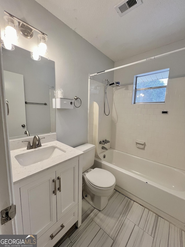 full bathroom with a textured ceiling, toilet, vanity, and tiled shower / bath