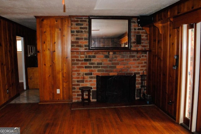 unfurnished living room with a brick fireplace, wood walls, a textured ceiling, and hardwood / wood-style flooring