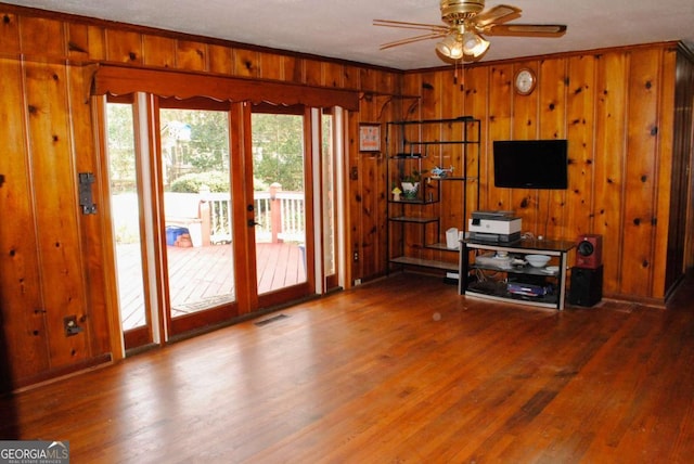 unfurnished living room with wooden walls, a textured ceiling, hardwood / wood-style floors, ceiling fan, and crown molding