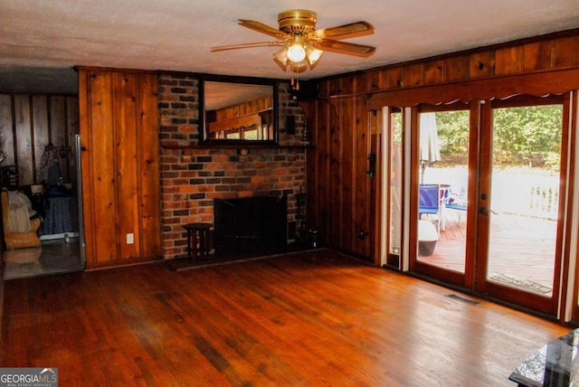 unfurnished living room with a textured ceiling, wood walls, hardwood / wood-style floors, a brick fireplace, and ceiling fan