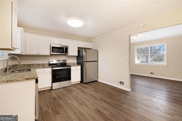 kitchen featuring appliances with stainless steel finishes, dark wood-type flooring, white cabinets, stone countertops, and sink