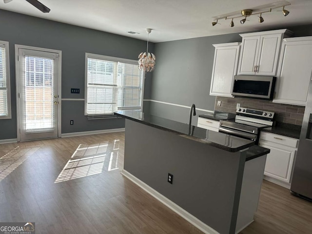 kitchen featuring decorative light fixtures, a kitchen island with sink, backsplash, white cabinetry, and appliances with stainless steel finishes