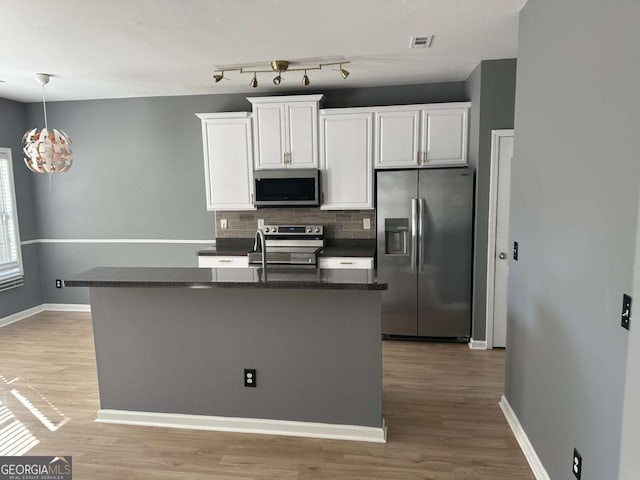 kitchen featuring decorative backsplash, white cabinetry, an island with sink, and appliances with stainless steel finishes