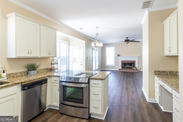 kitchen with appliances with stainless steel finishes, white cabinets, ceiling fan with notable chandelier, a brick fireplace, and dark wood-type flooring