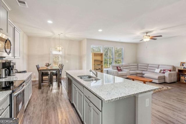 kitchen featuring light hardwood / wood-style flooring, pendant lighting, a center island with sink, appliances with stainless steel finishes, and sink