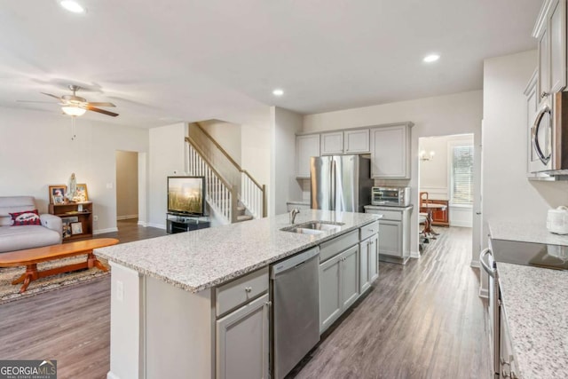 kitchen featuring stainless steel appliances, gray cabinets, a center island with sink, and hardwood / wood-style flooring