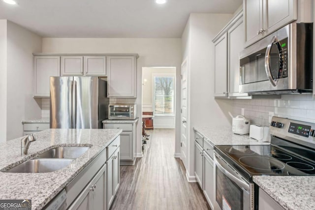 kitchen with stainless steel appliances, sink, hardwood / wood-style flooring, light stone countertops, and gray cabinets