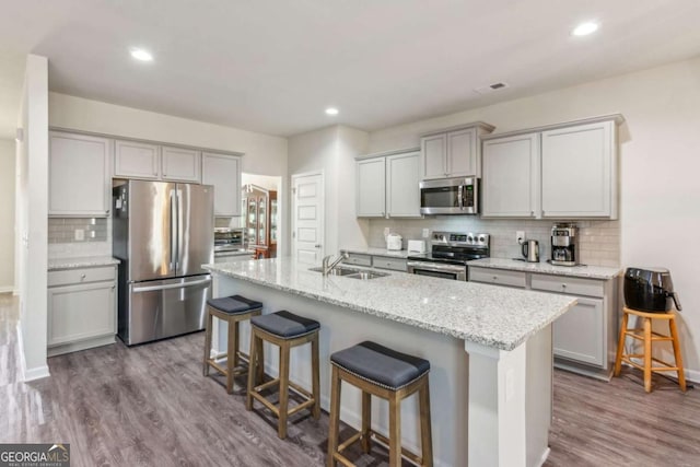 kitchen featuring light stone counters, hardwood / wood-style floors, appliances with stainless steel finishes, a kitchen breakfast bar, and sink