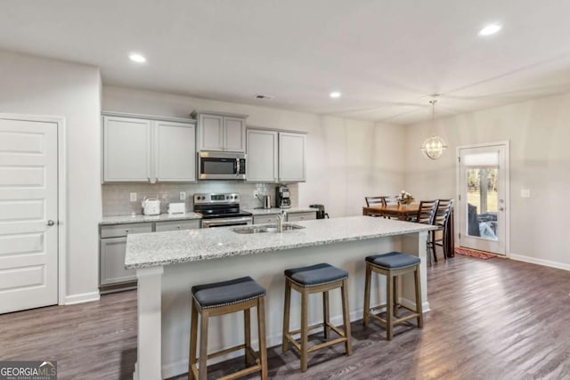 kitchen with a center island with sink, gray cabinets, light stone counters, and appliances with stainless steel finishes