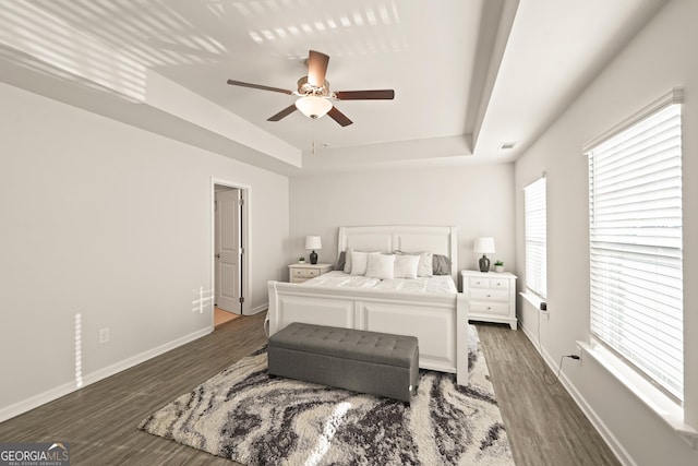 bedroom with ceiling fan, dark hardwood / wood-style floors, and a raised ceiling