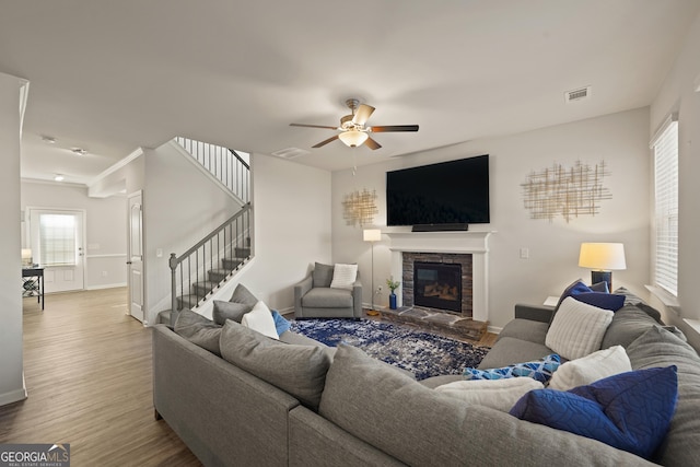 living room with ceiling fan, a stone fireplace, and hardwood / wood-style floors