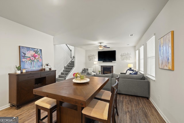 dining space featuring ceiling fan, a stone fireplace, and hardwood / wood-style floors