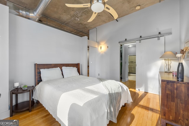 bedroom featuring ceiling fan, ensuite bath, light wood-type flooring, and a barn door