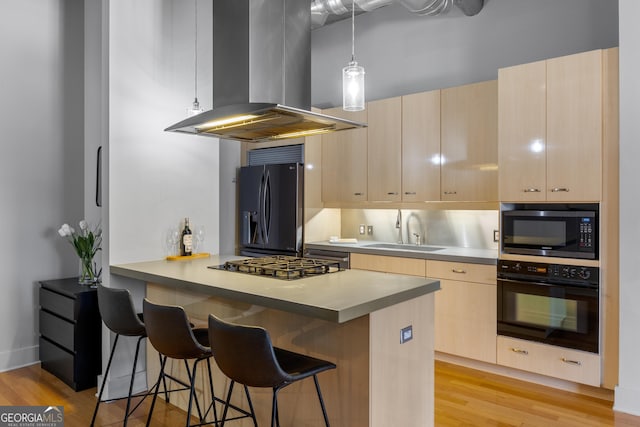 kitchen featuring light brown cabinetry, a breakfast bar, island exhaust hood, black appliances, and sink