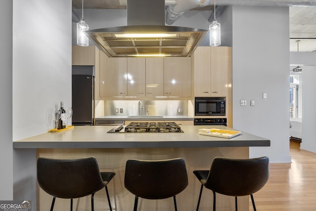 kitchen with built in appliances, pendant lighting, island range hood, light brown cabinets, and sink