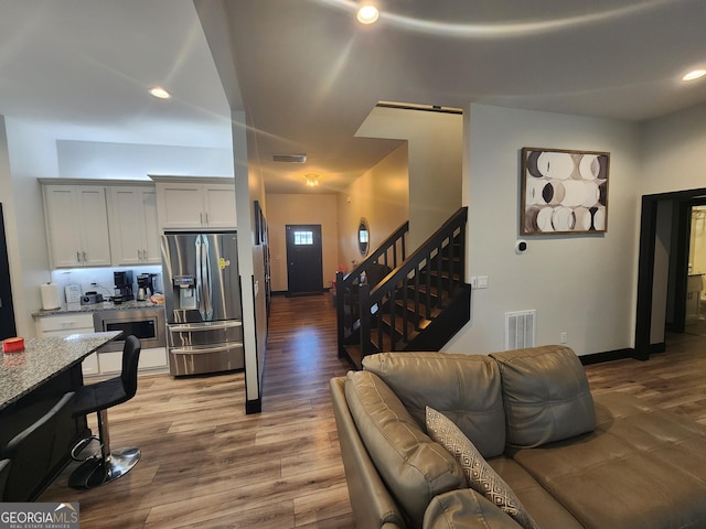 living room with recessed lighting, wood finished floors, visible vents, and stairs