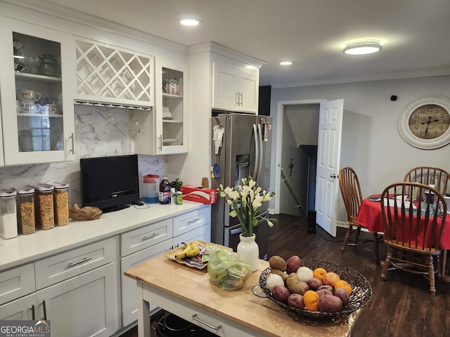 kitchen with stainless steel refrigerator with ice dispenser, ornamental molding, backsplash, and white cabinets