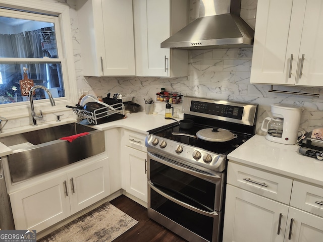 kitchen featuring range with two ovens, white cabinetry, sink, and wall chimney exhaust hood