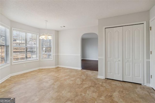 unfurnished dining area featuring a healthy amount of sunlight, a textured ceiling, and a chandelier