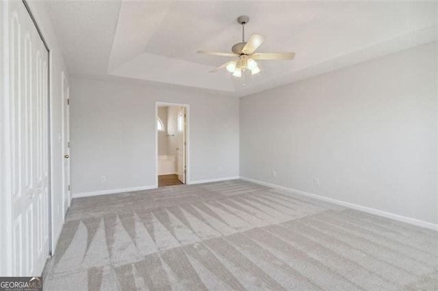 unfurnished bedroom featuring a raised ceiling, a closet, connected bathroom, light colored carpet, and ceiling fan