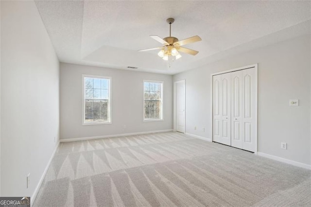 empty room featuring light carpet, ceiling fan, a textured ceiling, and a tray ceiling