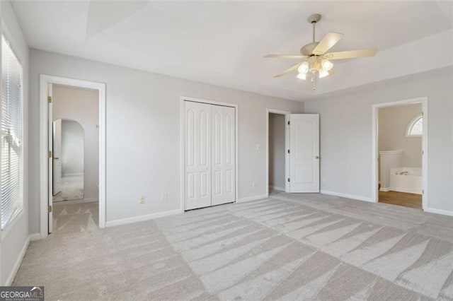 unfurnished bedroom with ensuite bathroom, light colored carpet, ceiling fan, and multiple windows