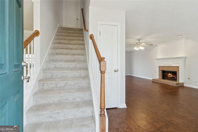 stairway featuring a fireplace, ceiling fan, and wood-type flooring