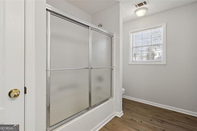 bathroom with toilet, bath / shower combo with glass door, and hardwood / wood-style floors