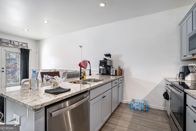 kitchen featuring stainless steel appliances, sink, light stone counters, kitchen peninsula, and gray cabinetry