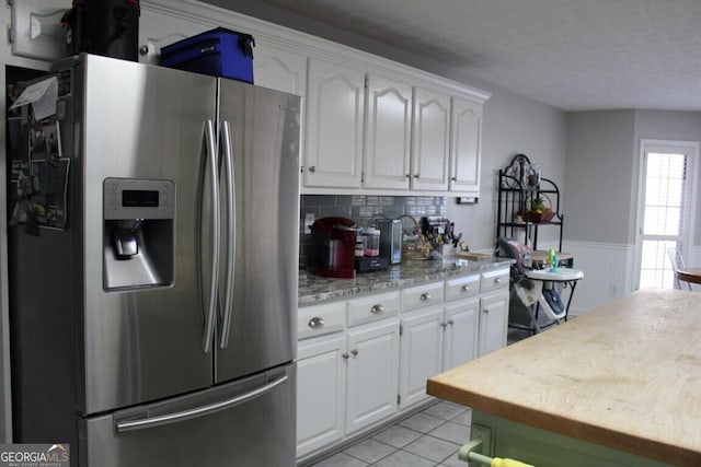 kitchen featuring stainless steel refrigerator with ice dispenser, light tile patterned floors, white cabinets, and light stone countertops