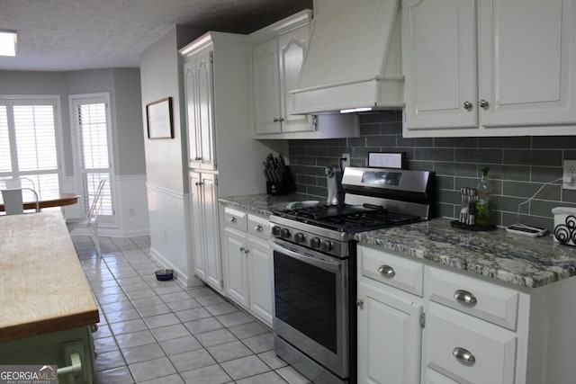 kitchen with light tile patterned floors, stainless steel range with gas cooktop, white cabinetry, and premium range hood