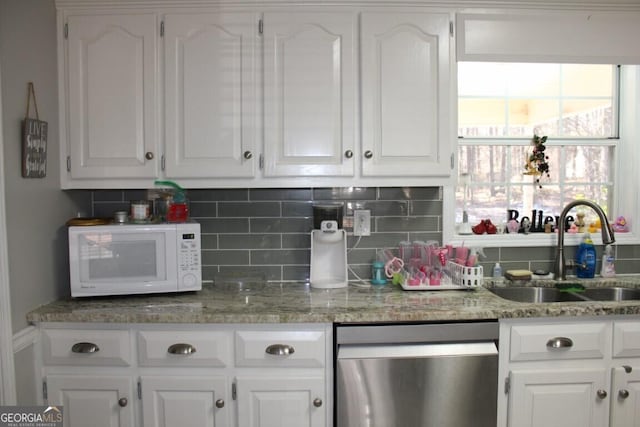 kitchen featuring stainless steel dishwasher, white cabinets, light stone counters, and sink