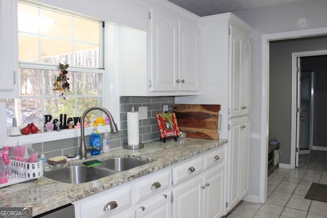 kitchen featuring light tile patterned floors, white cabinetry, tasteful backsplash, light stone countertops, and sink