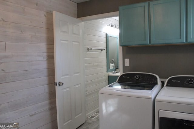 laundry room featuring cabinets, separate washer and dryer, wooden walls, and sink