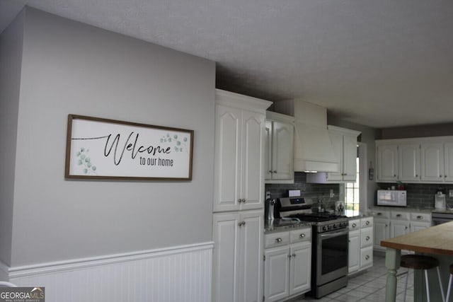 kitchen featuring stainless steel gas range, white cabinetry, and backsplash