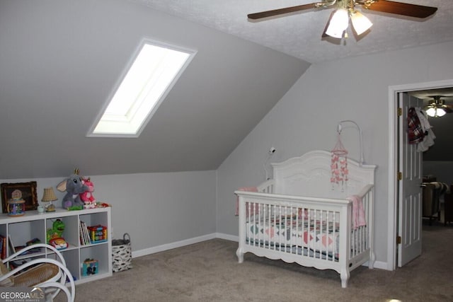 bedroom with ceiling fan, lofted ceiling with skylight, a crib, carpet flooring, and a textured ceiling