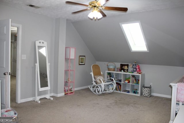 game room with light carpet, ceiling fan, vaulted ceiling with skylight, and a textured ceiling