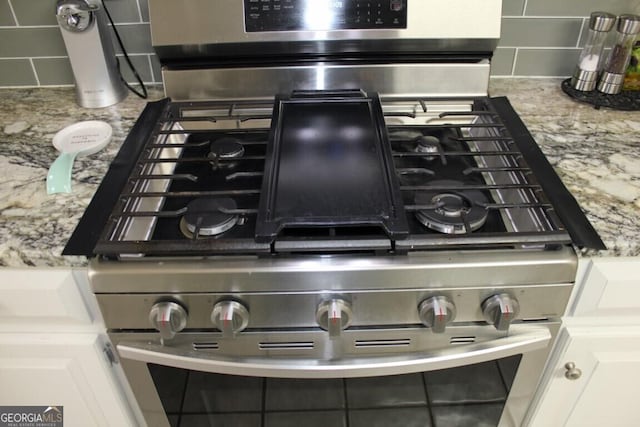 details with white cabinets, gas stove, and tasteful backsplash