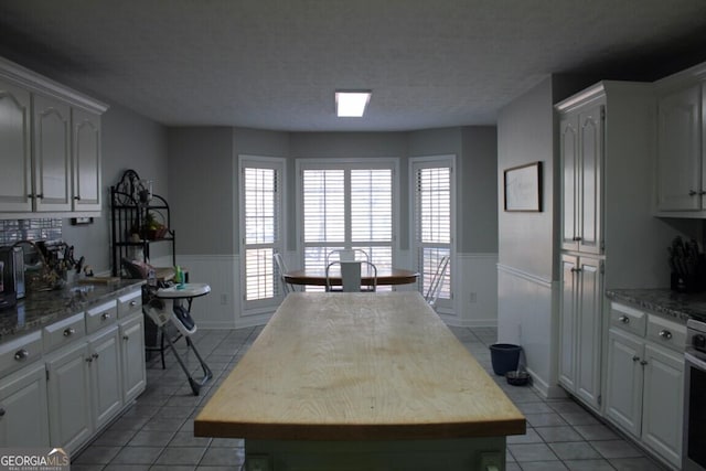 kitchen with white cabinets, light tile patterned flooring, a kitchen island, and range