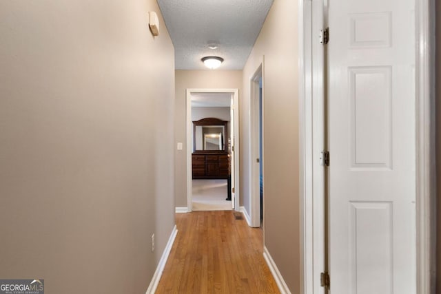 hallway with a textured ceiling and light hardwood / wood-style flooring