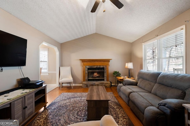 living room featuring a textured ceiling, a fireplace, lofted ceiling, ceiling fan, and light hardwood / wood-style floors