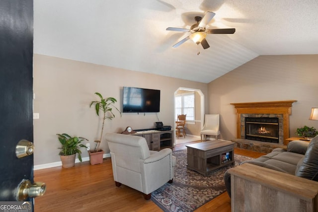 living room with lofted ceiling, hardwood / wood-style flooring, ceiling fan, and a stone fireplace