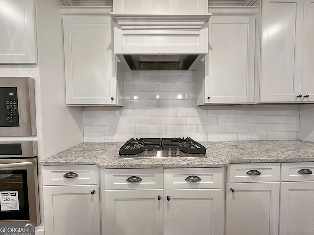 kitchen featuring stainless steel appliances, custom range hood, light stone counters, white cabinets, and tasteful backsplash