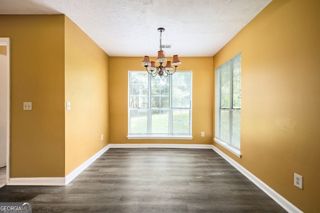 unfurnished dining area featuring dark wood-type flooring, a textured ceiling, and a chandelier