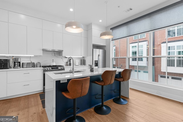 kitchen with pendant lighting, sink, a kitchen island with sink, stainless steel appliances, and white cabinets