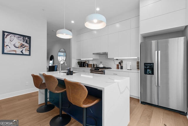 kitchen featuring white cabinetry, a center island with sink, stainless steel appliances, backsplash, and hanging light fixtures