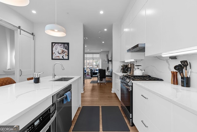 kitchen featuring decorative light fixtures, a barn door, dishwasher, gas range, and light stone counters