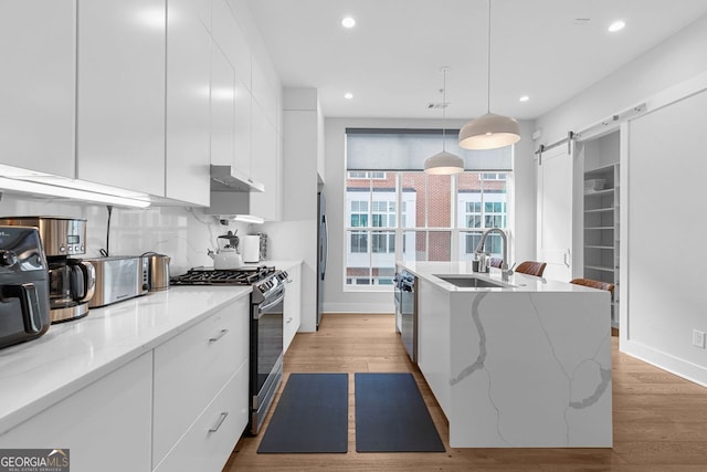 kitchen with pendant lighting, white cabinetry, stainless steel appliances, sink, and a barn door